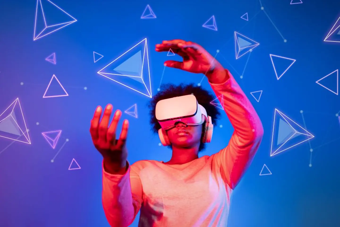 Mulher com óculos de realidade virtual em frente a um fundo azul e rosa olhando para formas geométricas flutuantes