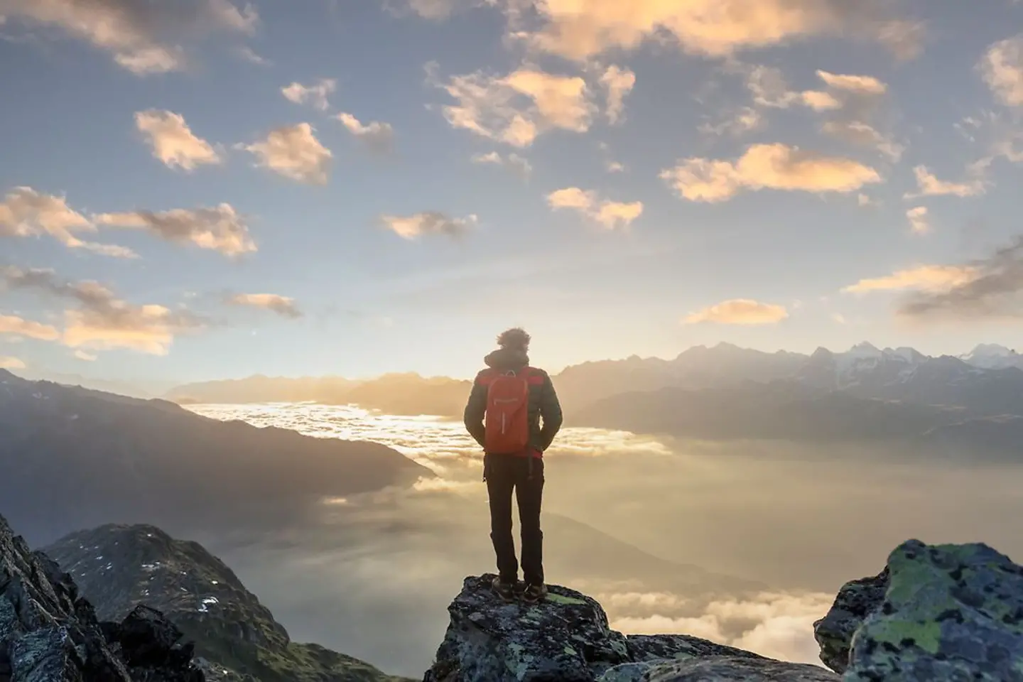 Hombre con mochila de pie en una montaña viendo cómo sale el sol