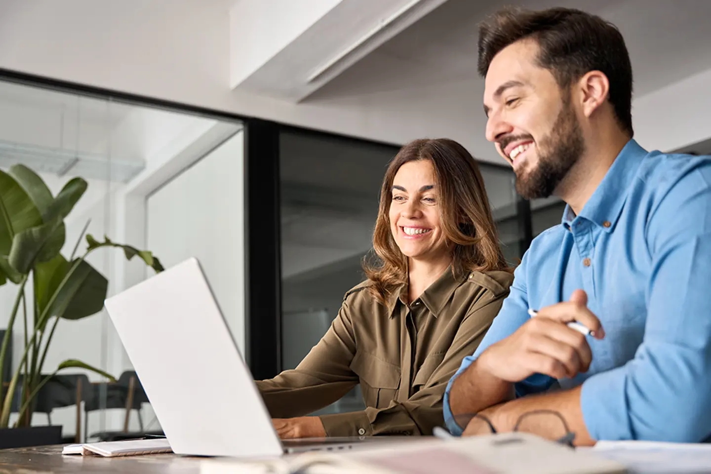 Dois profissionais sorridentes em uma conversa, trabalhando com laptops no escritório